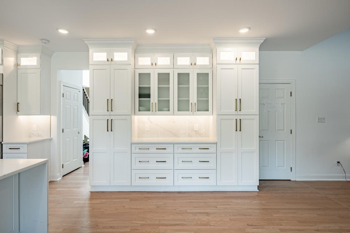 Kitchen perimeter cabinetry with white shaker doors, brushed gold pulls, under-cabinet lighting, and quartz countertops