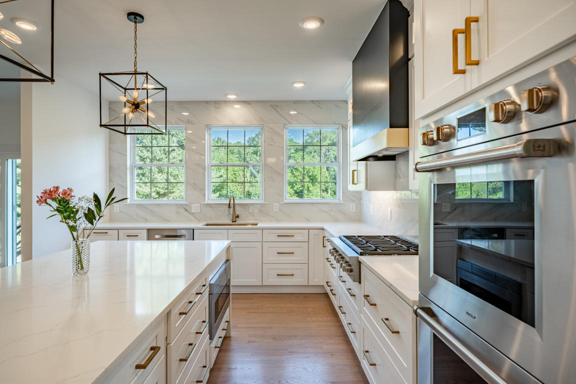 Sink wall with three windows, gold undermount sink, pull-down sprayer faucet, and marble-look tile backsplash