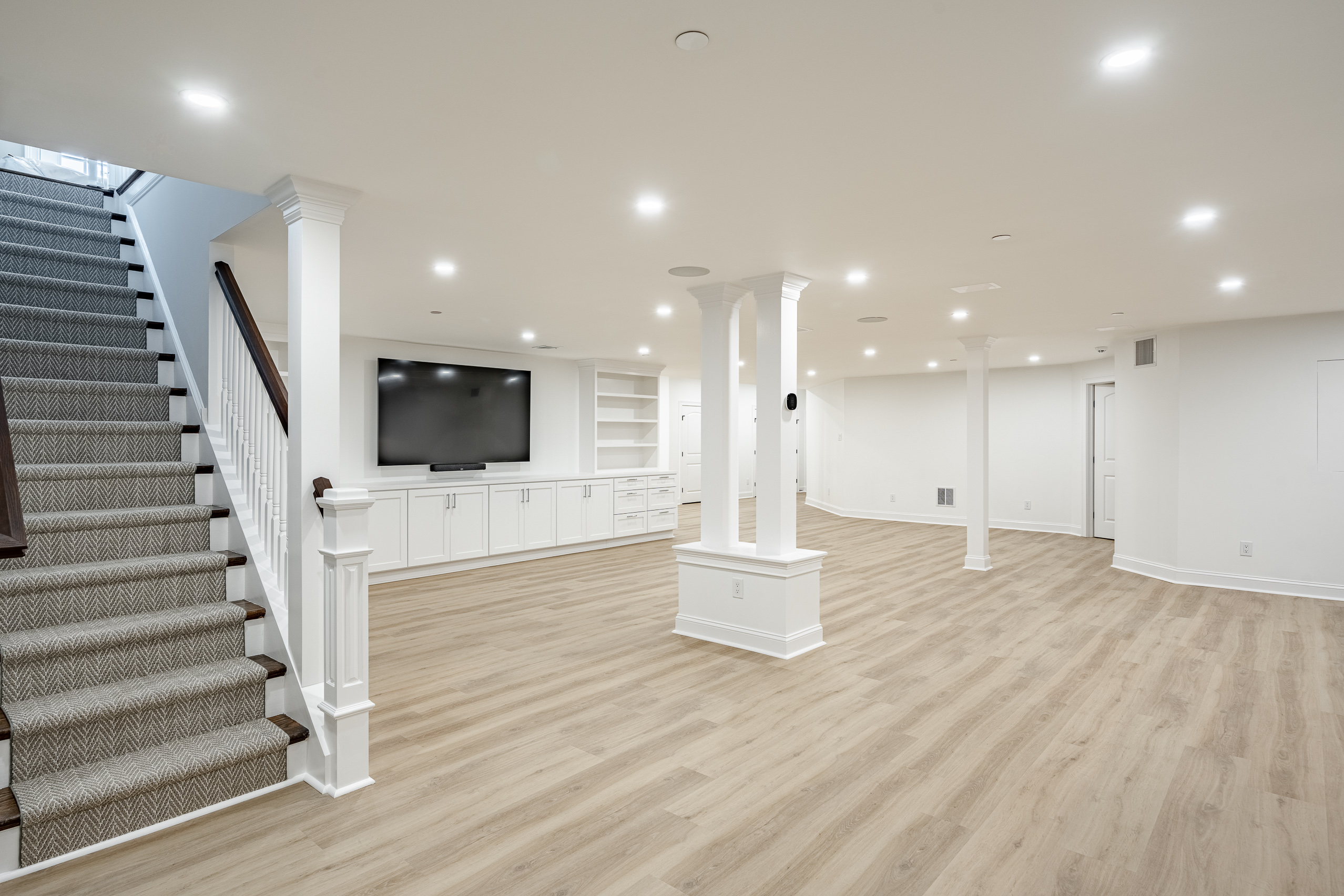 Newtown Square basement remodel by Craftsworth Construction - spacious main living area with entertainment center, columns, and staircase