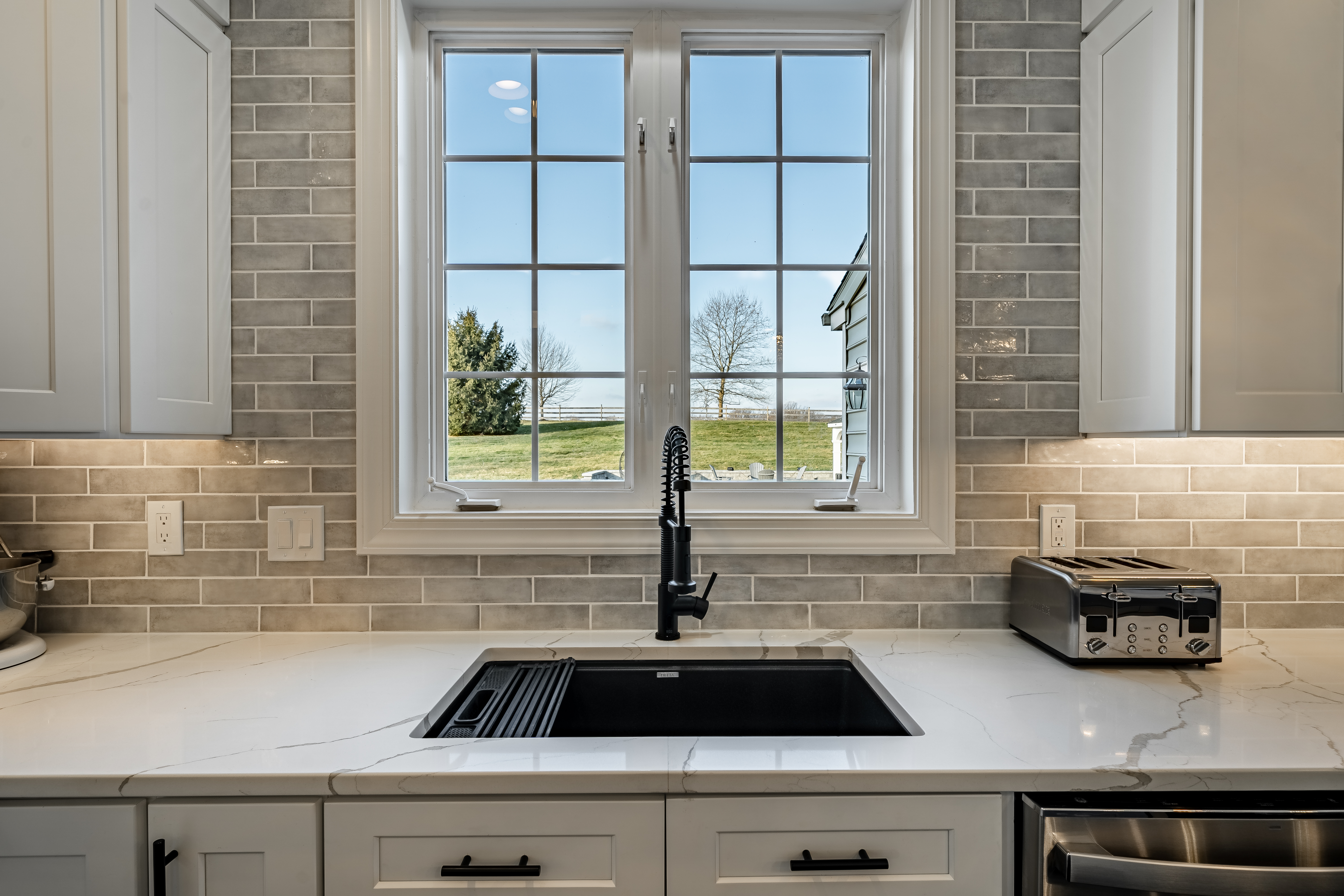 Kitchen sink detail - matte black undermount workstation sink with pull-down faucet, quartz countertop, and window overlooking Chester County landscape