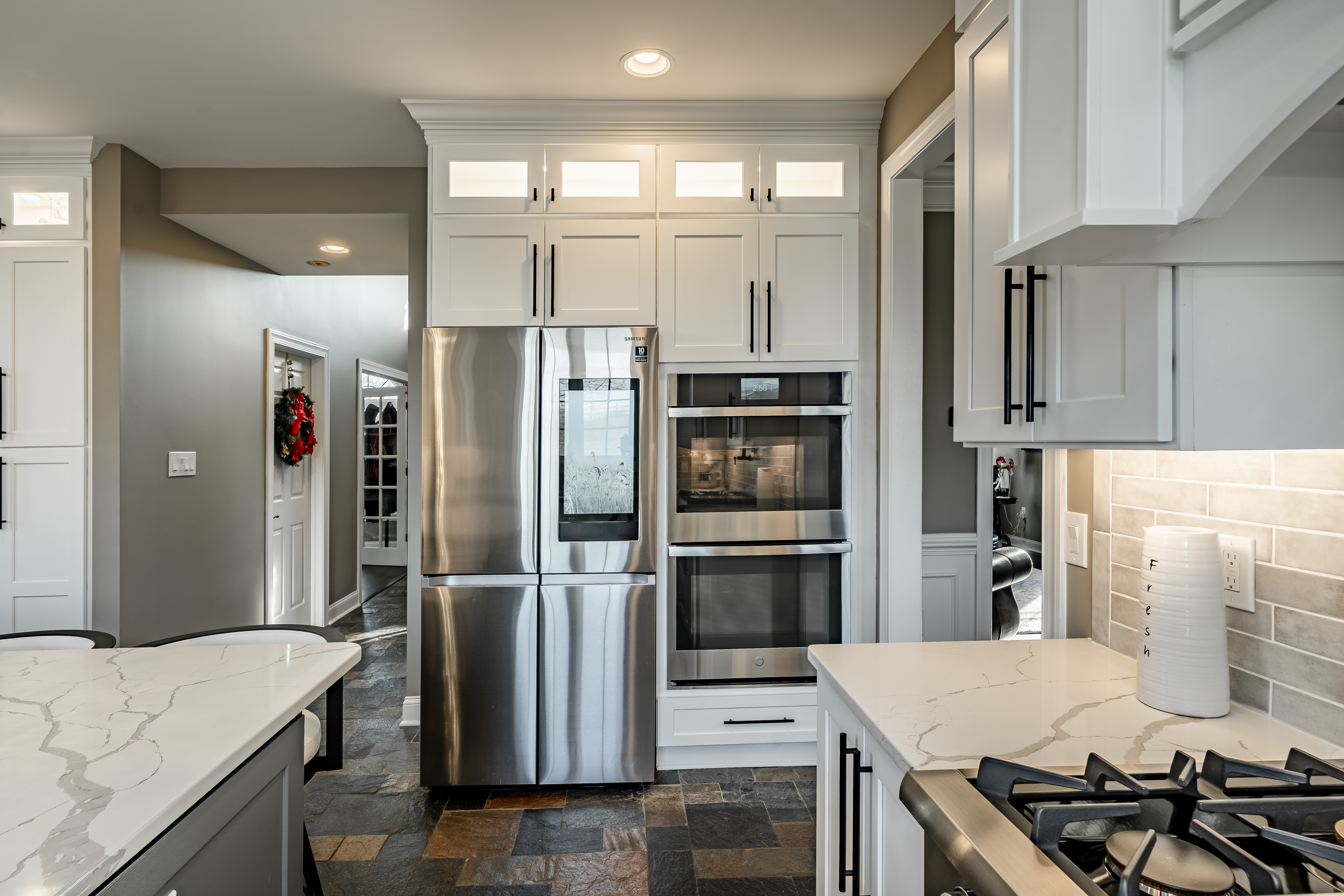 West Brandywine kitchen appliance wall - Samsung four-door refrigerator and built-in wall oven with floor-to-ceiling white cabinetry and glass transoms