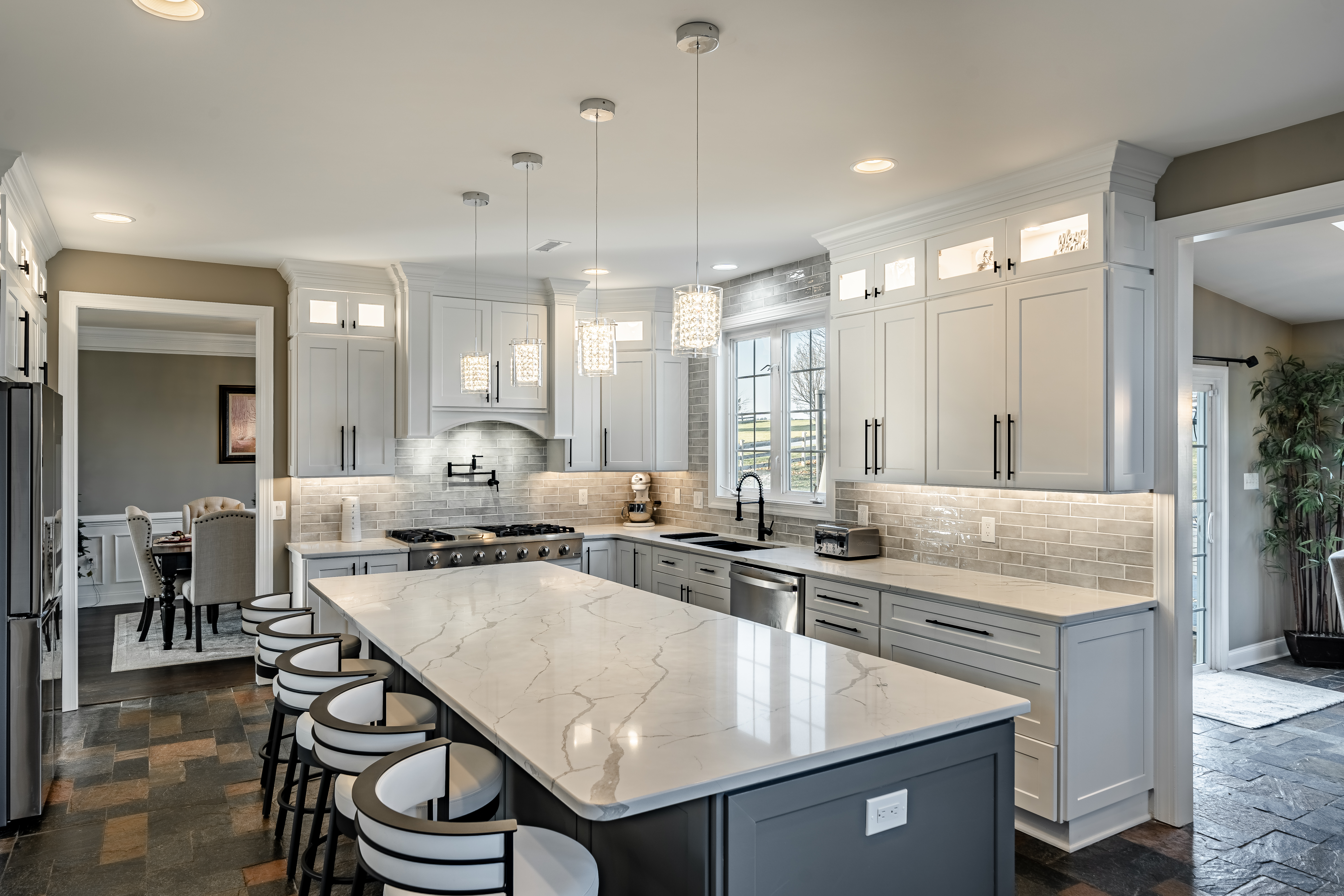 West Brandywine kitchen remodel by Craftsworth Construction - wide angle view of two-tone kitchen with dark gray island, white shaker cabinets, quartz countertops, crystal pendant lights, and bar seating