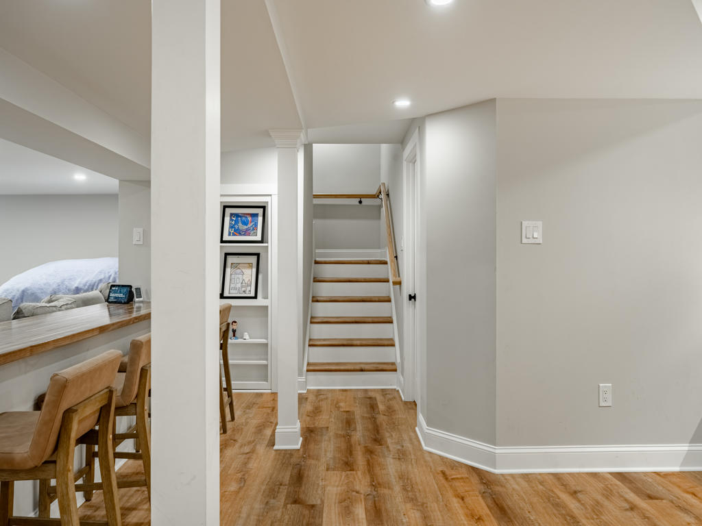 West Chester basement entry view showing LVP flooring, white columns, butcher block bar counter with bar stools, built-in shelving niche, and open staircase