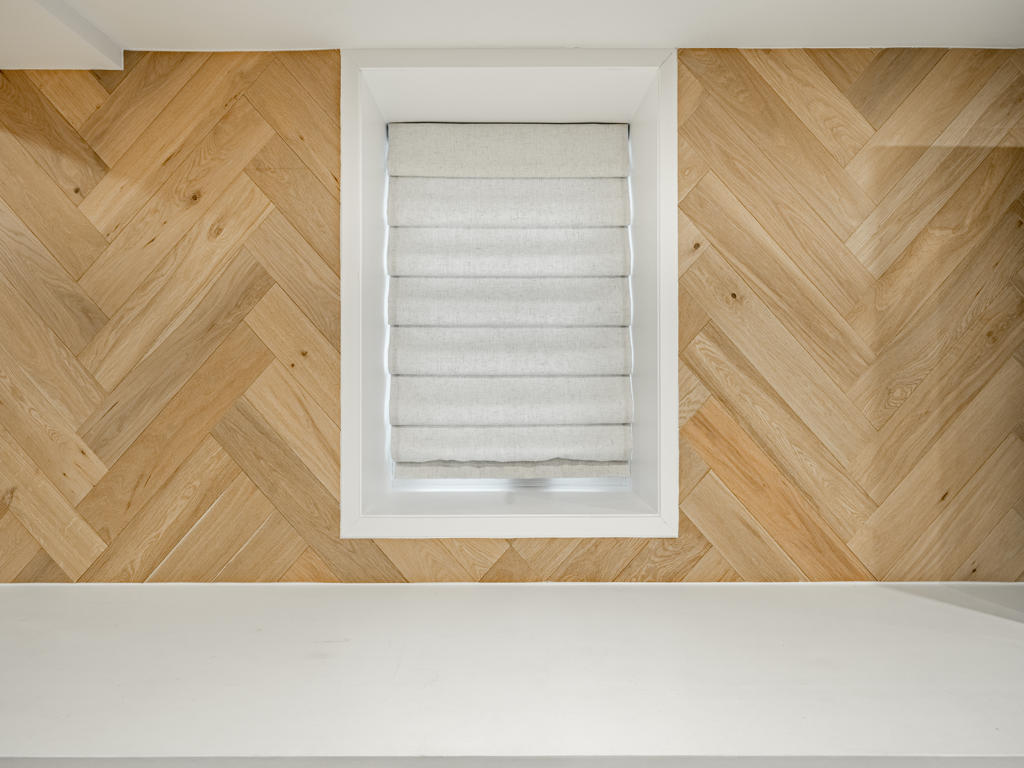 Detail of white oak herringbone plank pattern with egress window trimmed cleanly into wood surface on West Chester basement media wall