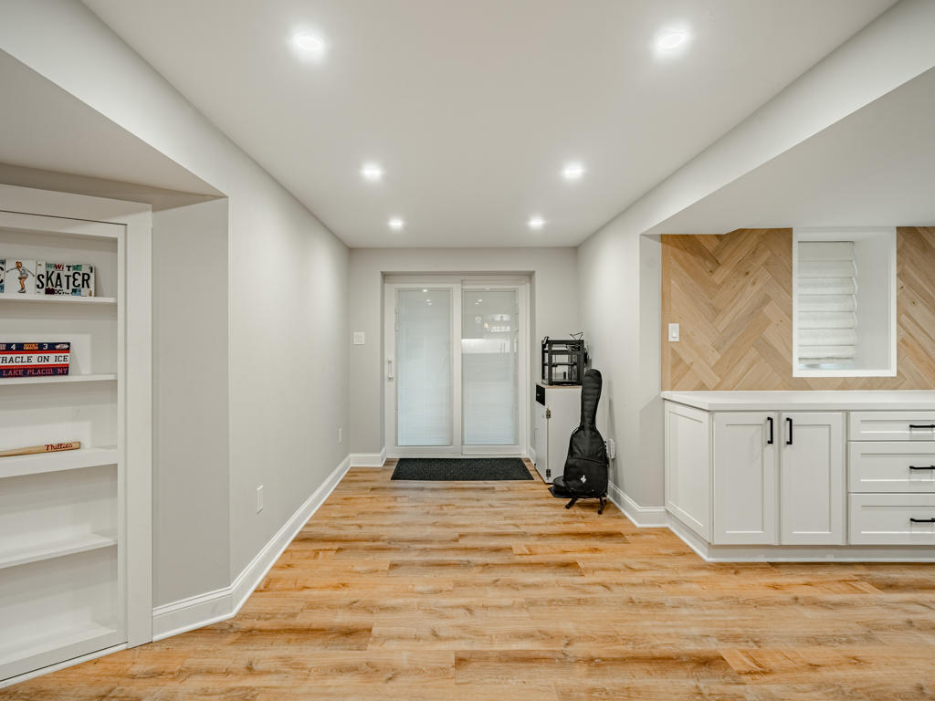 West Chester finished basement hallway showing egress door, built-in shelving, herringbone TV wall visible beyond, and LVP flooring throughout