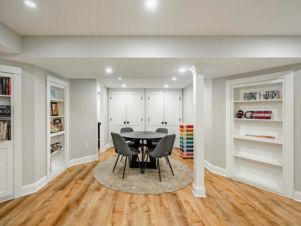 West Chester basement game room with round black table, gray chairs, custom built-in bookshelves flanking space, and white storage closet doors beyond