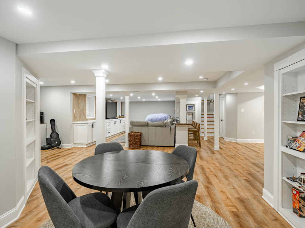 Full length view of West Chester PA basement renovation from game room end looking toward lounge, herringbone wall, and bar zone with all spaces visible