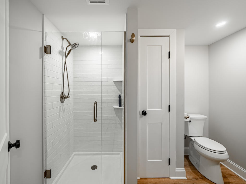Basement bathroom vanity in West Chester PA with dark cabinet, white quartz countertop, brushed gold faucet, round gold-framed mirror, and gold globe sconces