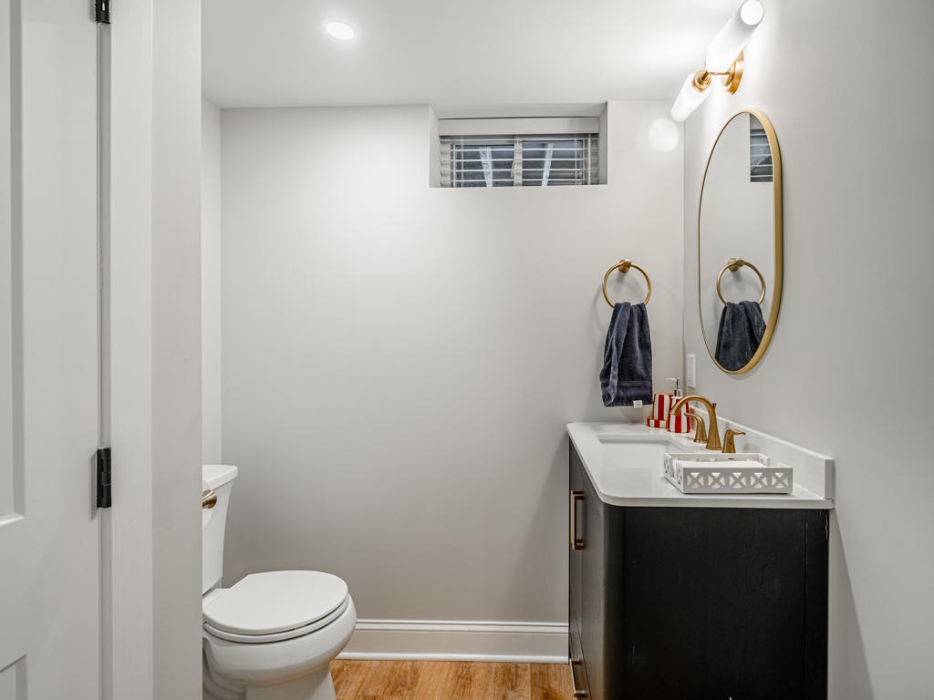 Full basement bathroom in West Chester PA with frameless glass shower, white subway tile, dark espresso vanity, white quartz top, round gold mirror, and globe sconces