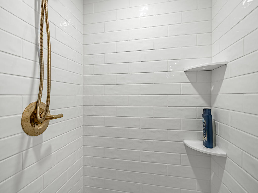 Interior of white subway tile shower with brushed gold handheld wand, built-in corner niche shelving, and frameless glass enclosure in West Chester basement bathroom