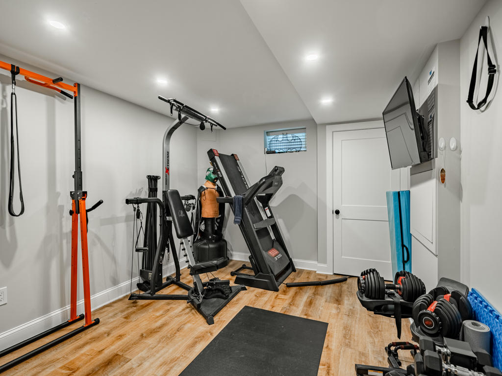 Dedicated home gym room in West Chester finished basement with recessed lighting, LVP flooring, wall-mounted TV, treadmill, cable machine, and free weights