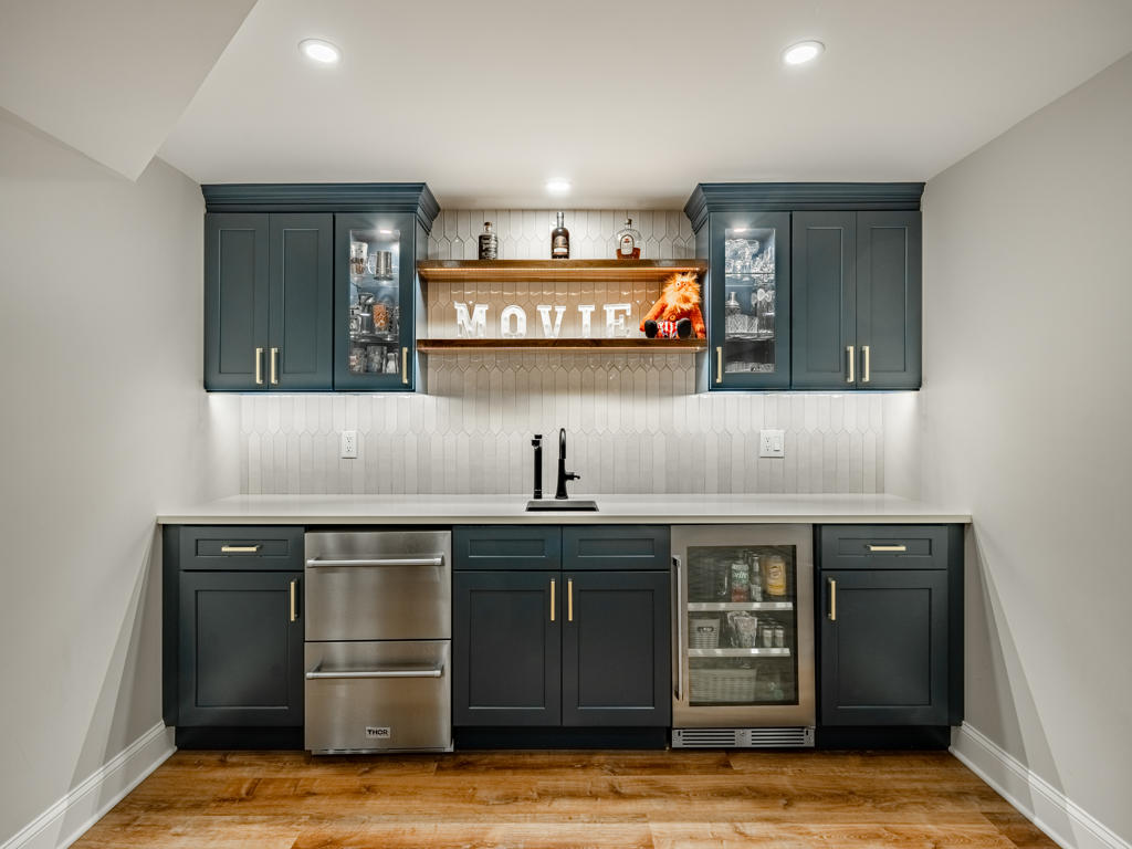 Navy shaker wet bar with Thor appliances, glass-front cabinets, live-edge floating shelf, and white picket tile backsplash in West Chester basement remodel