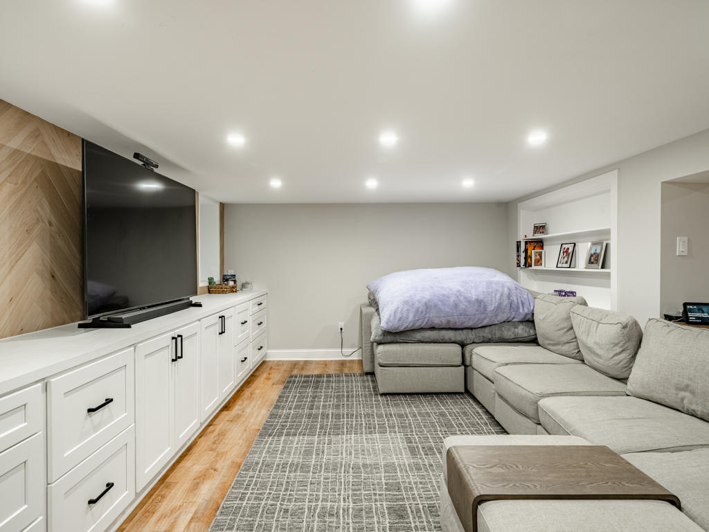 Media wall in West Chester basement showing herringbone white oak, large TV, soundbar, and full run of white built-in cabinetry from wall to wall