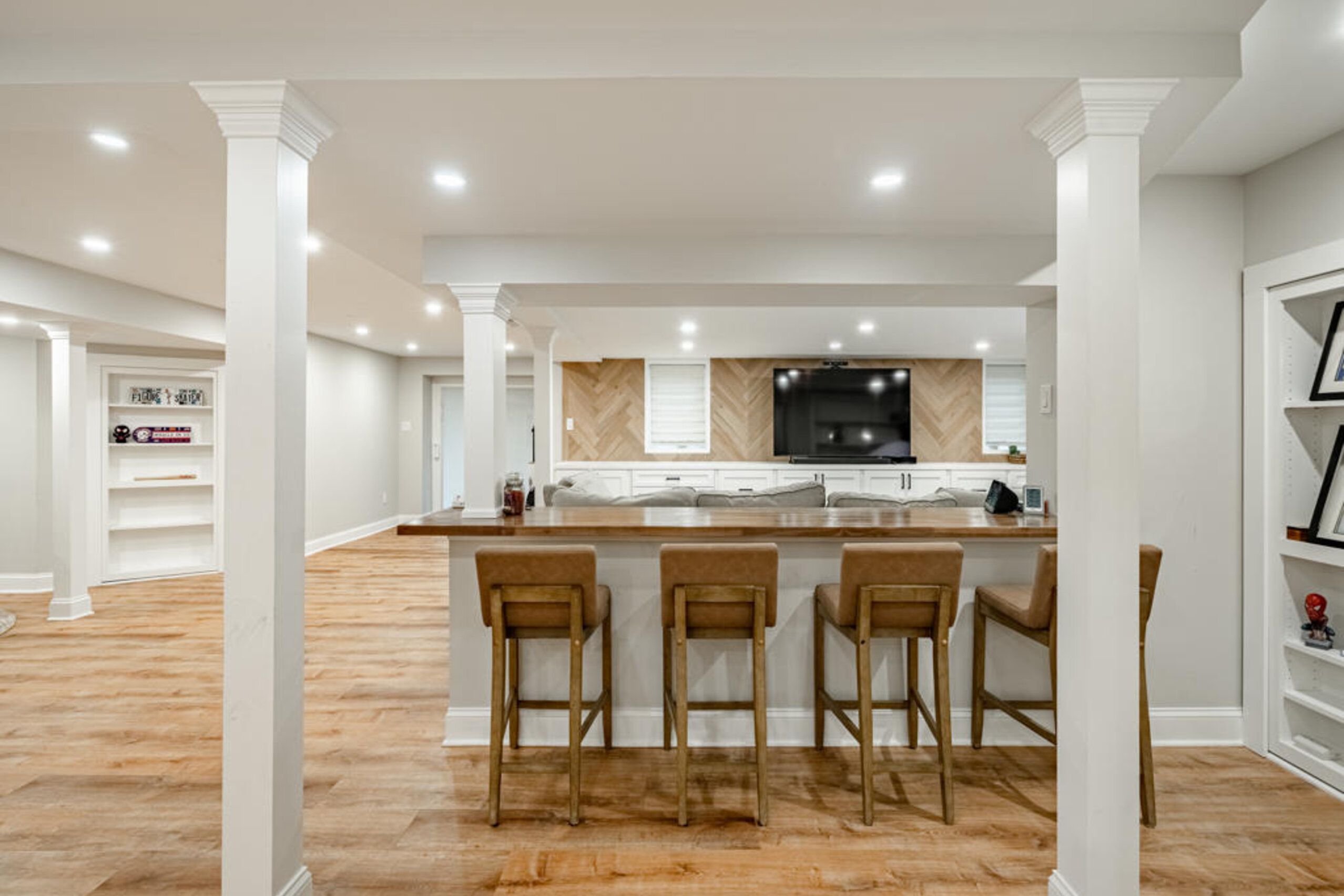 West Chester PA basement remodel with white oak herringbone accent wall, navy bar, hidden bookshelf doors, and butcher block bar counter