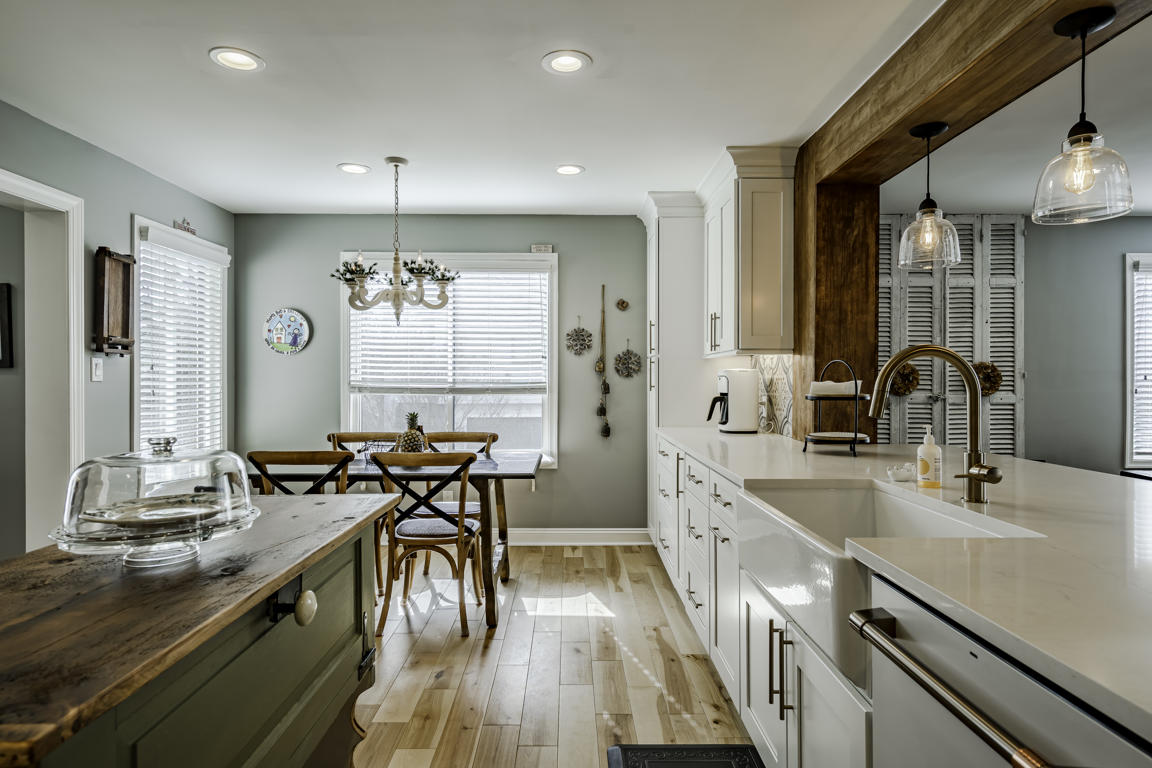 West Chester farmhouse kitchen remodel by Craftsworth Construction - wide view of white shaker cabinets with decorative cement tile backsplash, quartz countertops, professional gas range, and custom white range hood