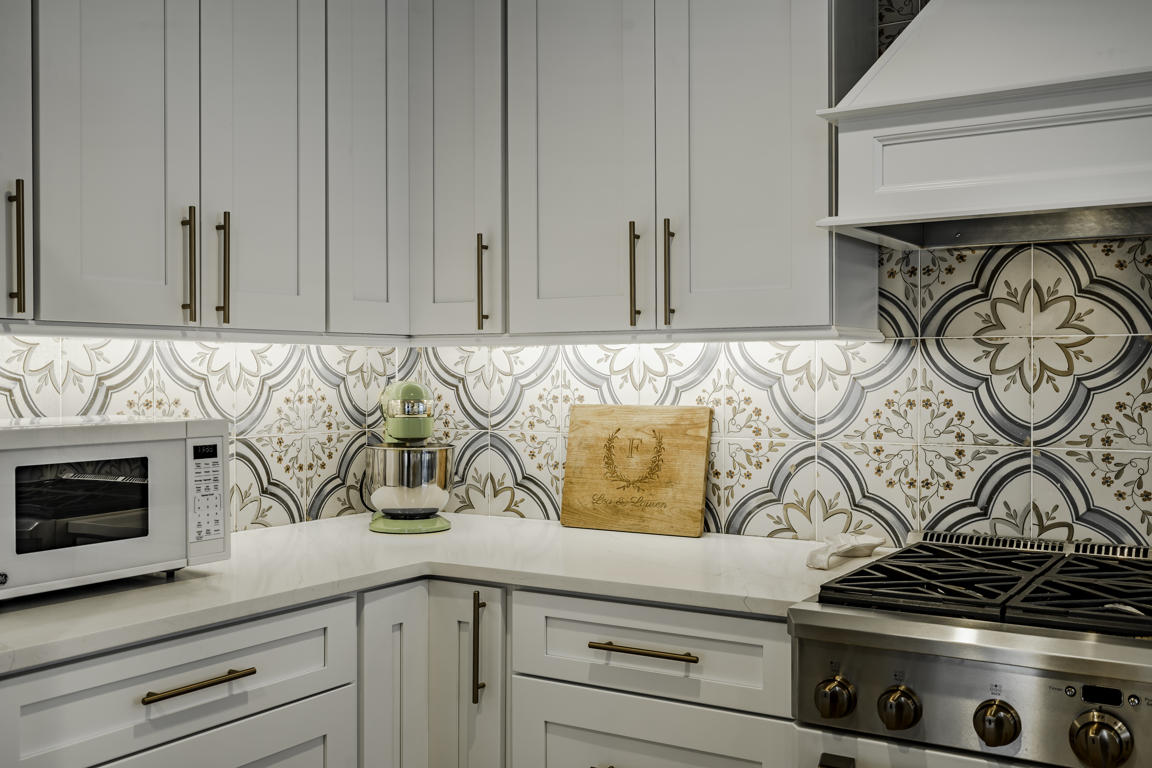 Kitchen wall oven and microwave built into white shaker cabinetry with brass knobs beside refrigerator alcove