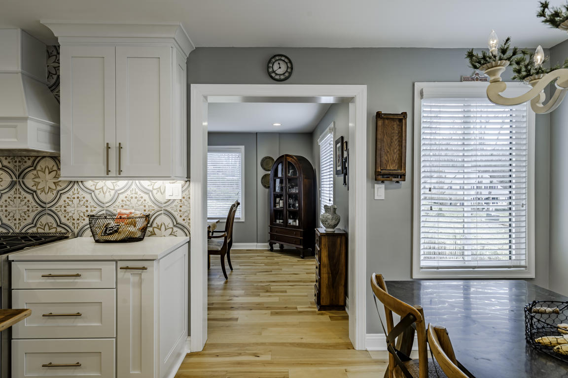 Kitchen from dining area angle showing white cabinetry, brass fixtures, and connection to adjacent living spaces