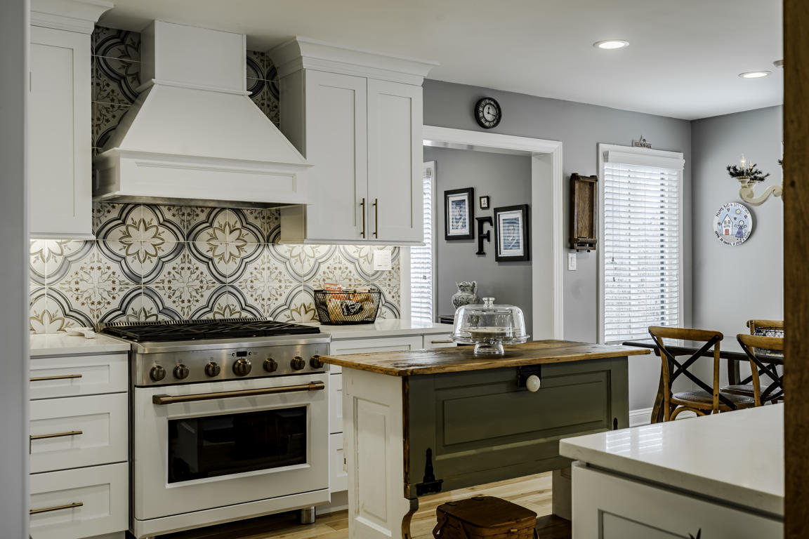 Full kitchen overview with hickory hardwood floors, white cabinets, gas range with hood, and glass pendant lights