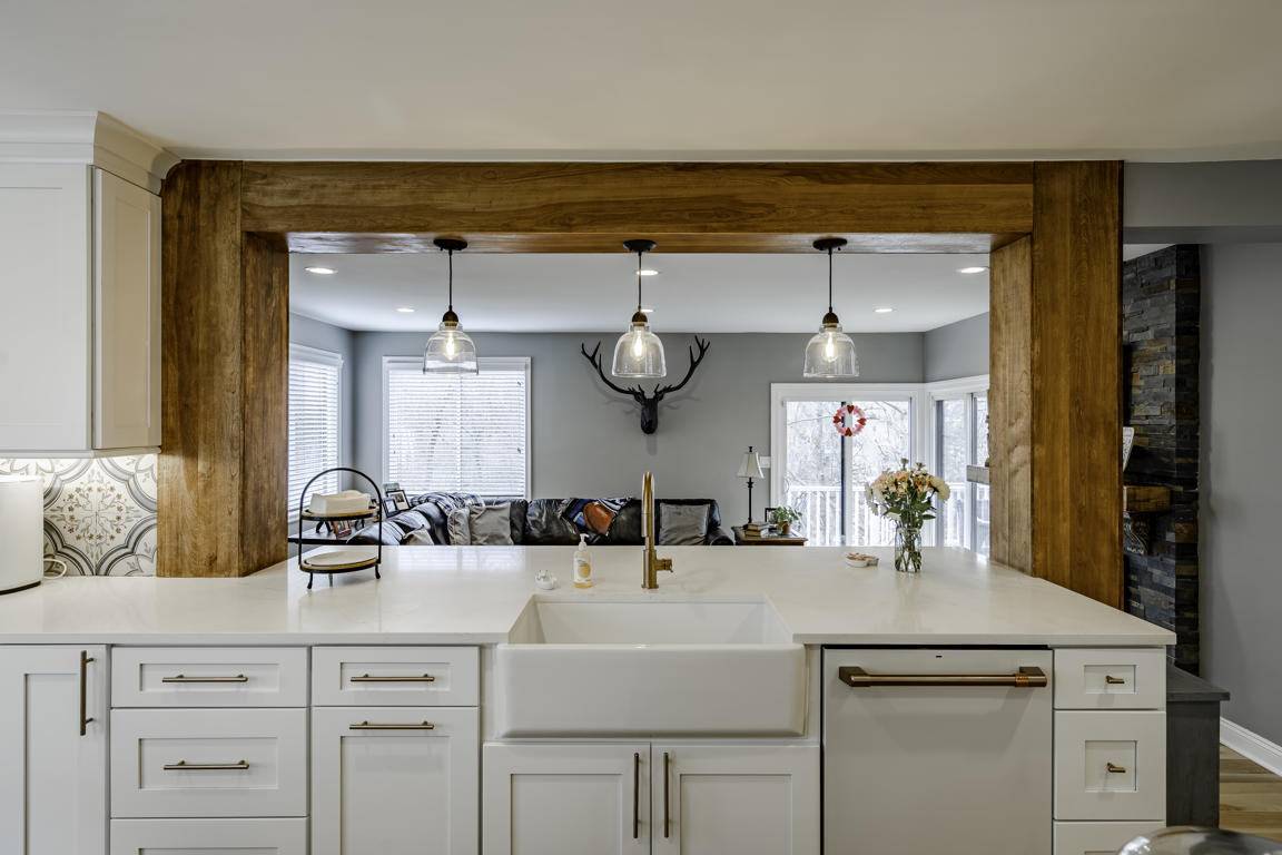 Dishwasher integrated into white cabinetry run beside deep farmhouse-style sink with brass faucet