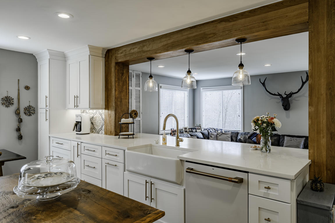 Family room viewed from kitchen with leather sectional sofa, industrial coffee table, and bar stools at peninsula