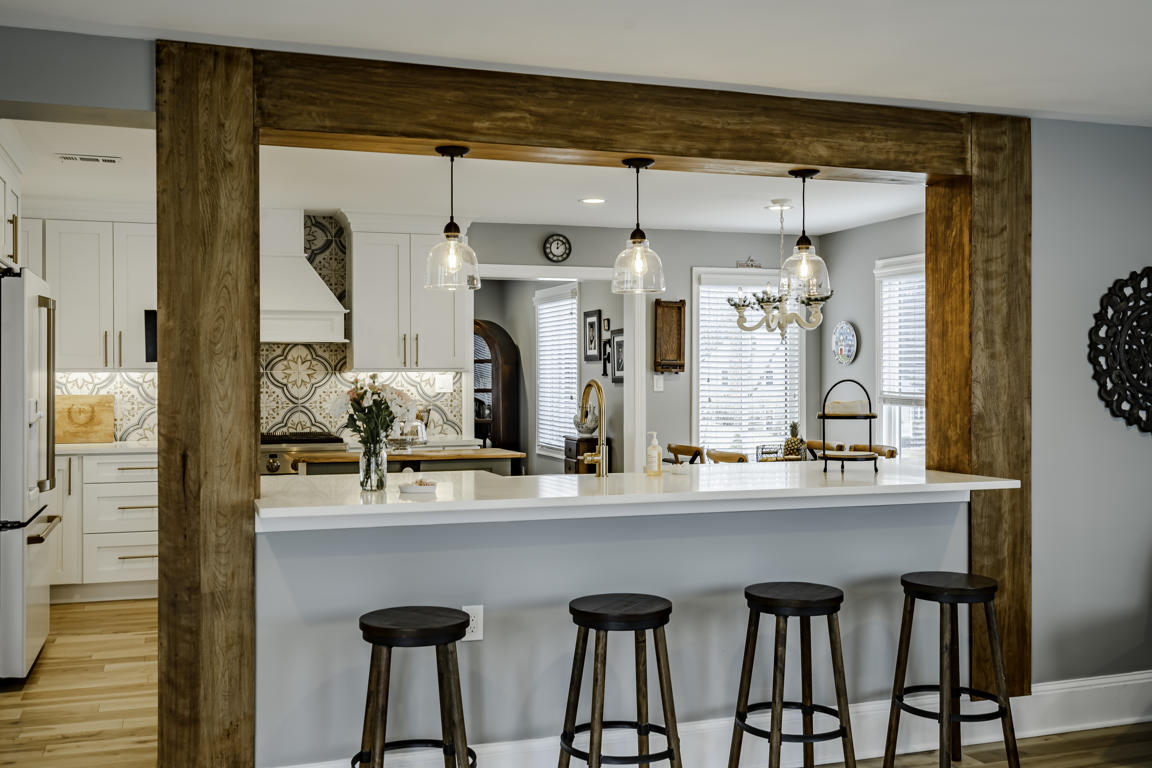Farmhouse kitchen from family room side showing exposed wood beam post, pendant lights, and white cabinetry