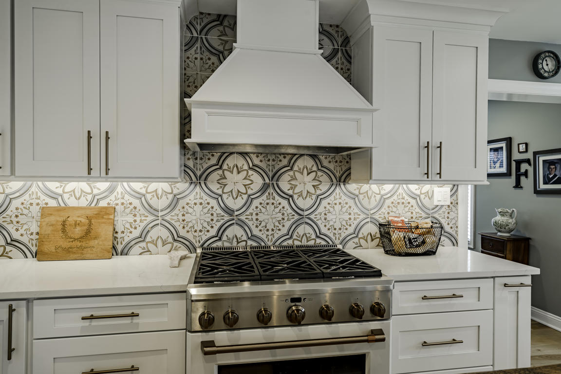 Kitchen range wall detail - professional gas range with custom white hood, geometric backsplash tile, and soft-close shaker cabinets