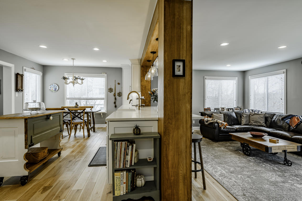 Kitchen to family room transition showing sage green island, book storage, exposed beam, and leather sectional beyond