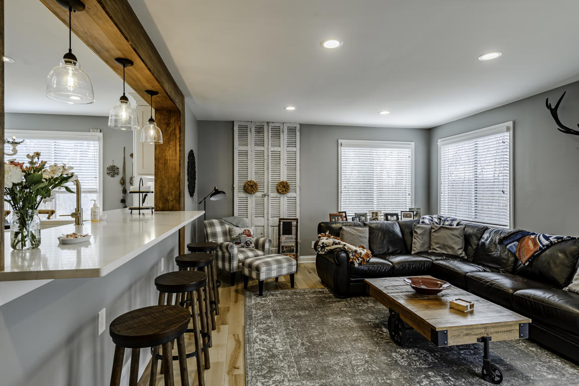 Family room from kitchen angle with bar stools at peninsula, glass pendant lights, louvered shutters, and leather sofa