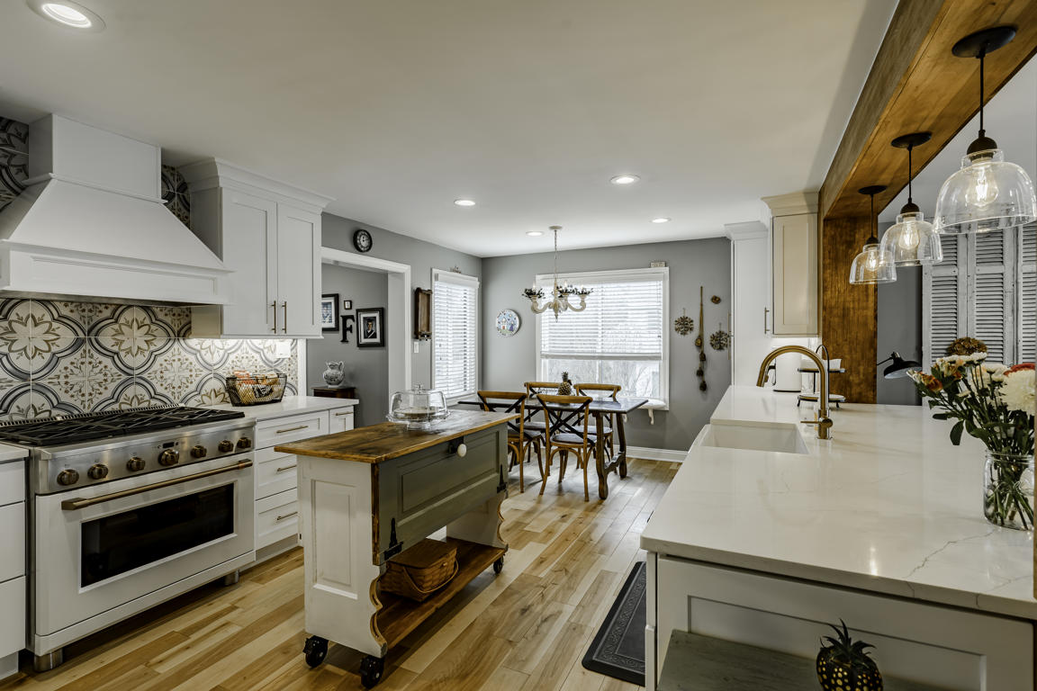 Full kitchen panorama showing range hood, cement tile backsplash, rolling island, pendant lights, and dining area