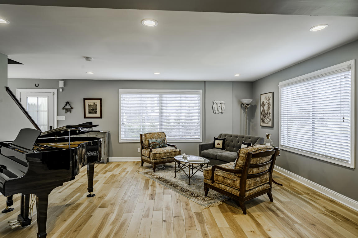 Living room with baby grand piano, upholstered armchairs, tufted sofa, and area rug on hickory hardwood floors
