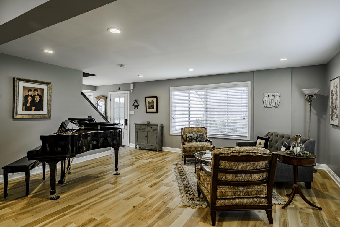 Living room wide angle showing baby grand piano, front entry door, stairway with wood handrail, and seating area