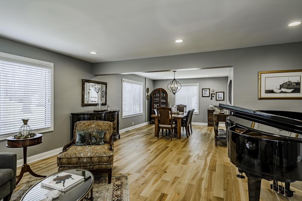 Living room looking toward dining room showing continuous hickory floors, gray walls, and ornate chandelier beyond