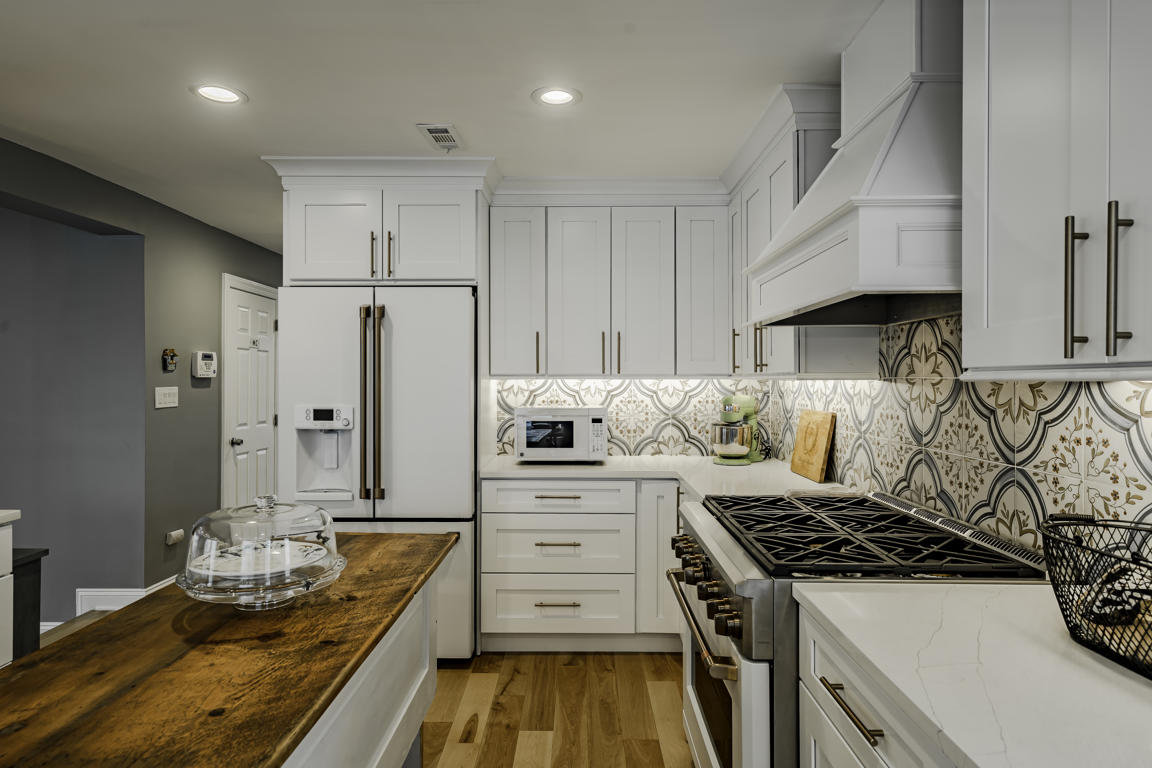 Brushed brass kitchen faucet with arched spout on quartz countertop, white shaker base cabinets and cement tile backsplash
