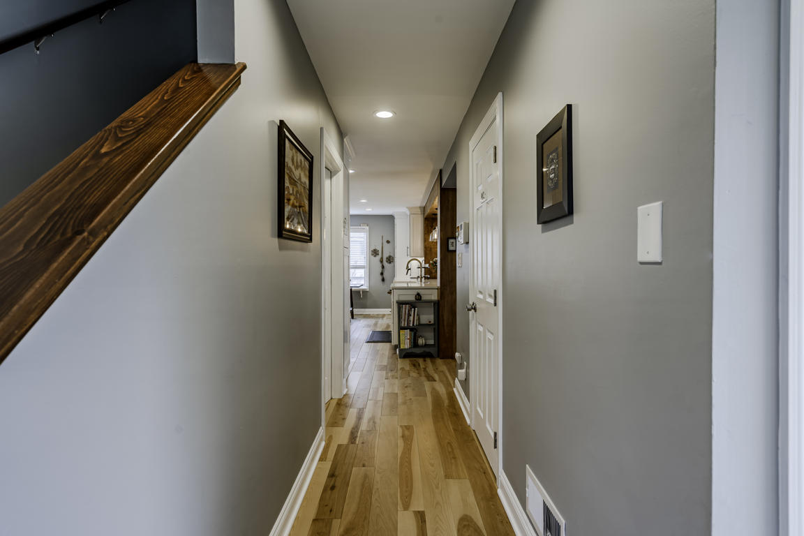 First-floor hallway with hickory hardwood floors, wood stair handrail, recessed lighting, and view to kitchen beyond