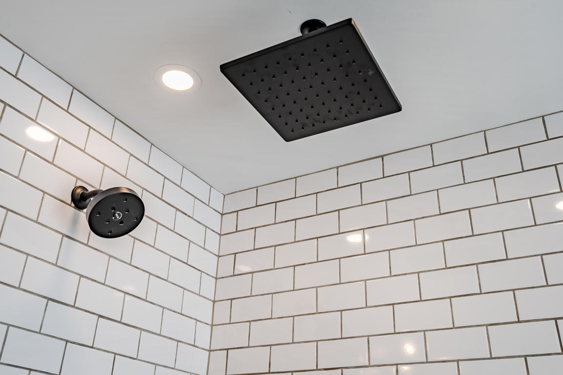 Matte black shower fixtures detail including square rainfall head, adjustable slide bar with handheld wand, and mixing valve