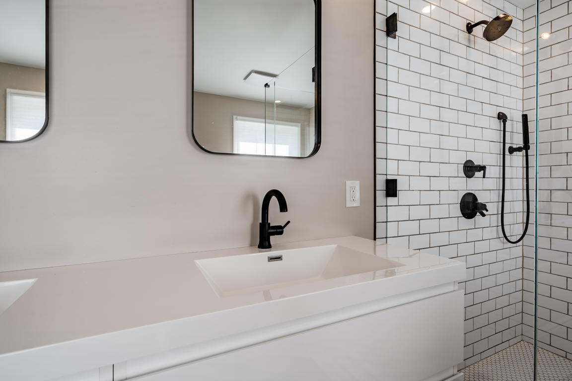 Frameless glass shower enclosure corner showing black hardware hinges and clips against white subway tile