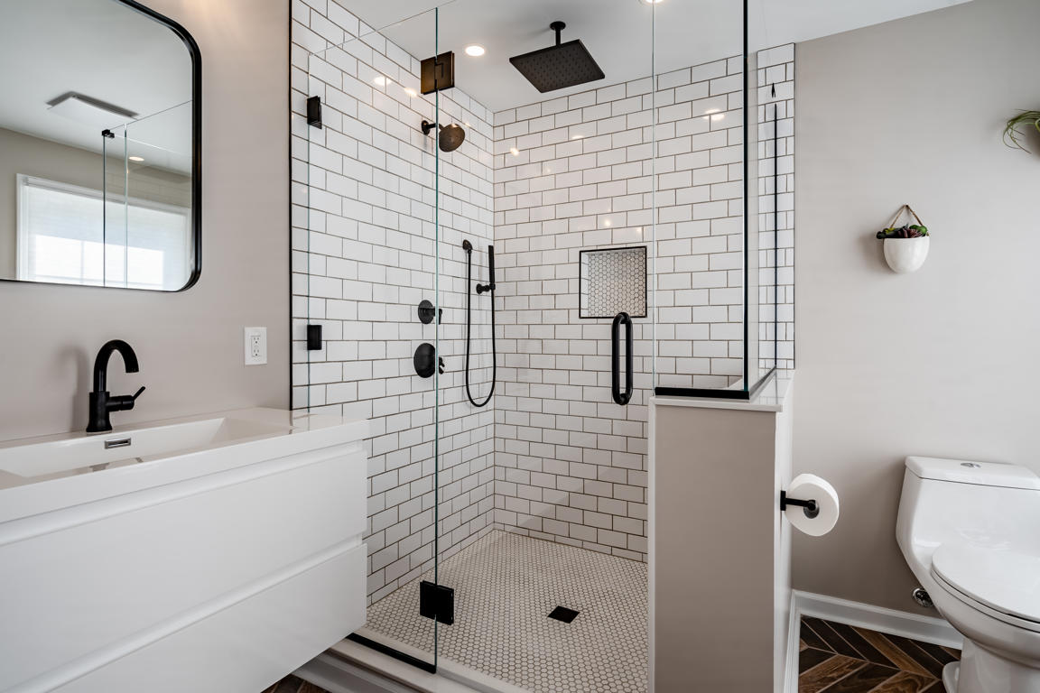 Soaking tub and accent cabinet vignette with natural window light, herringbone floor, and warm greige wall color