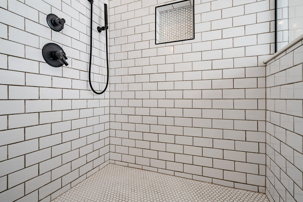 Floor-mounted matte black tub filler with gooseneck spout and handheld sprayer beside freestanding white tub