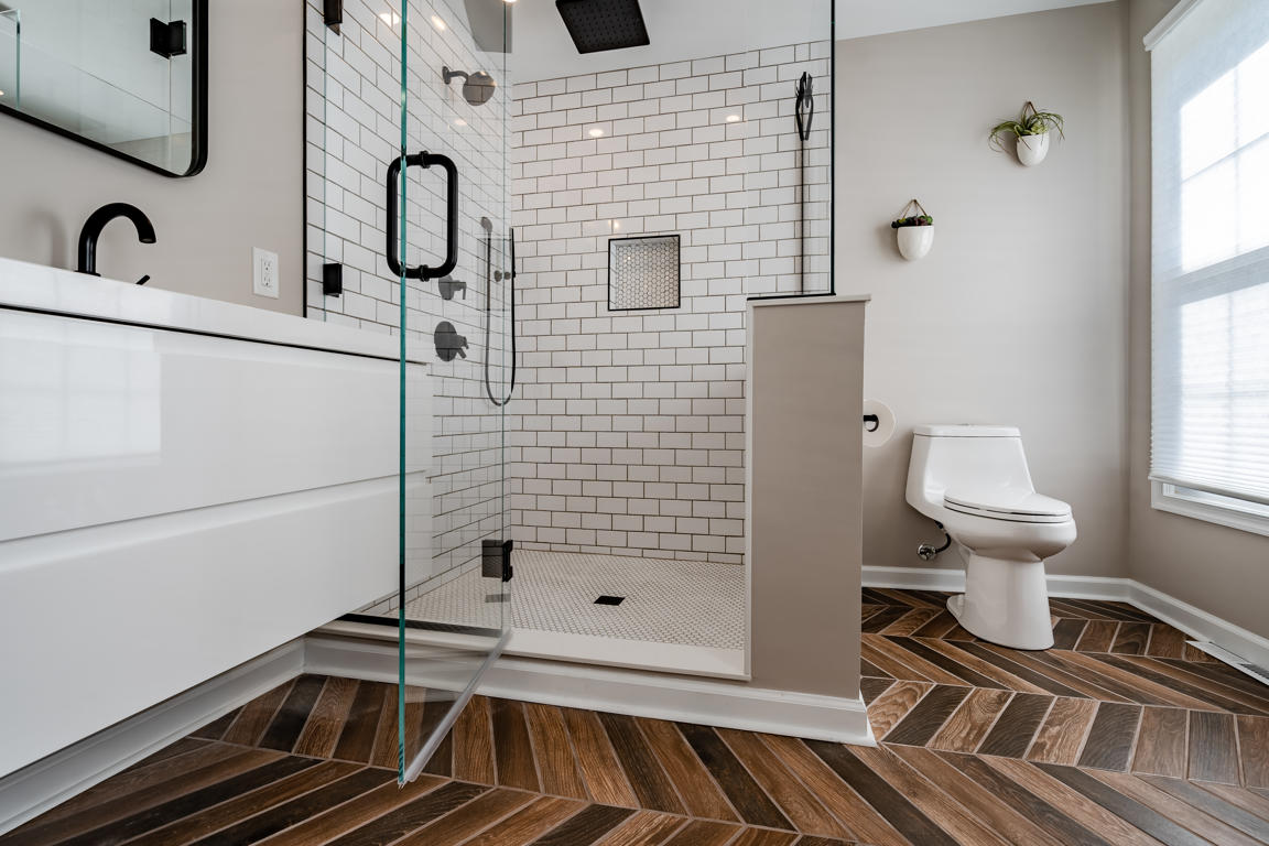 Shower and vanity relationship showing frameless glass, white subway tile pony wall, floating vanity, and herringbone floor