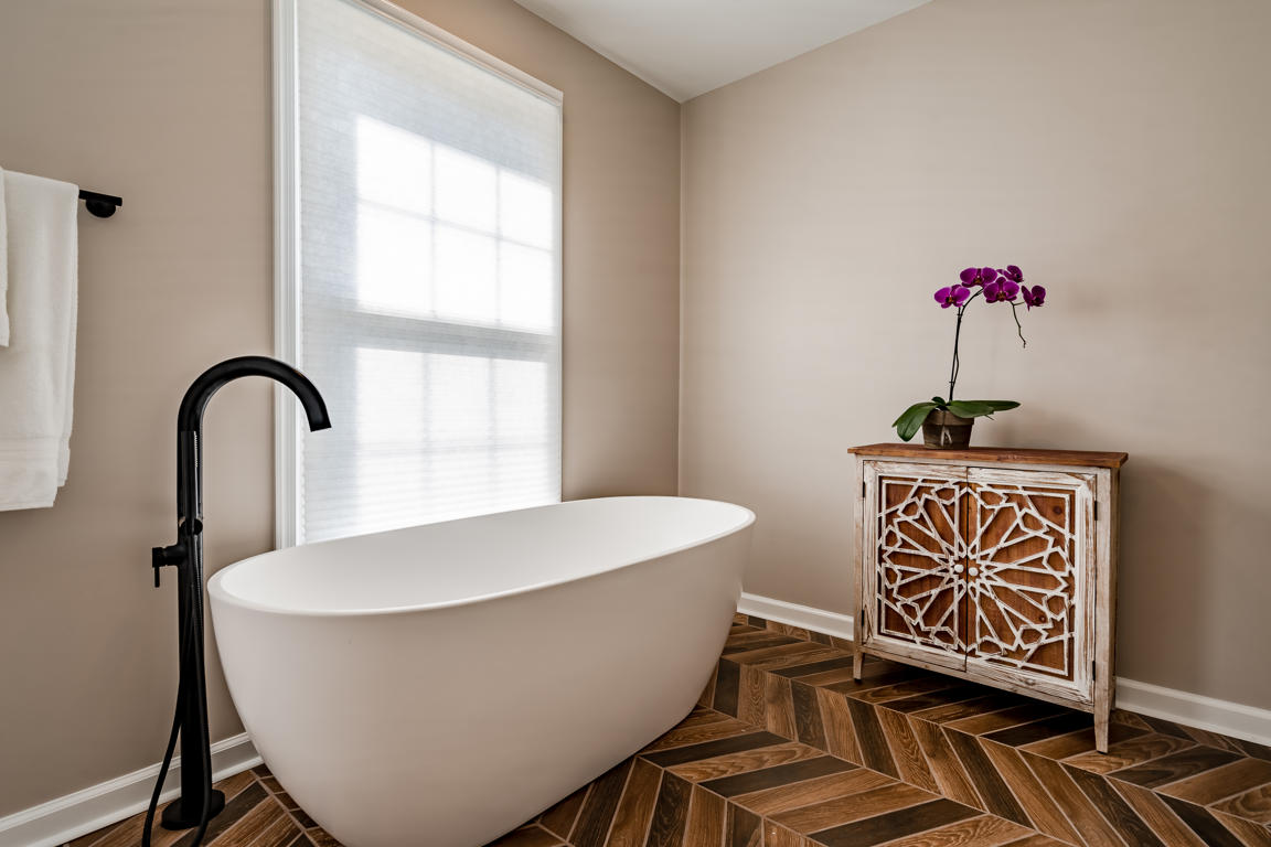 Soaking tub from alternate angle showing sculptural oval form against greige walls and herringbone tile floor