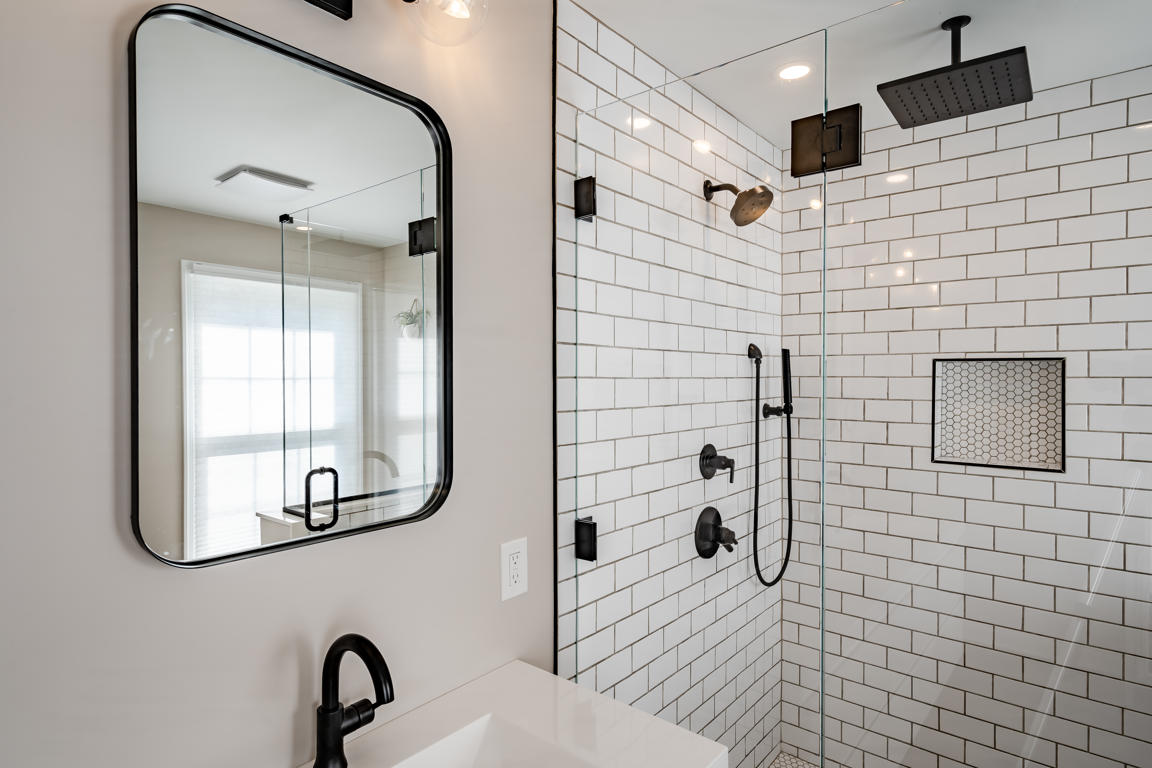 Black-framed mirror and matte black vanity faucet with white subway tile shower visible in mirror reflection
