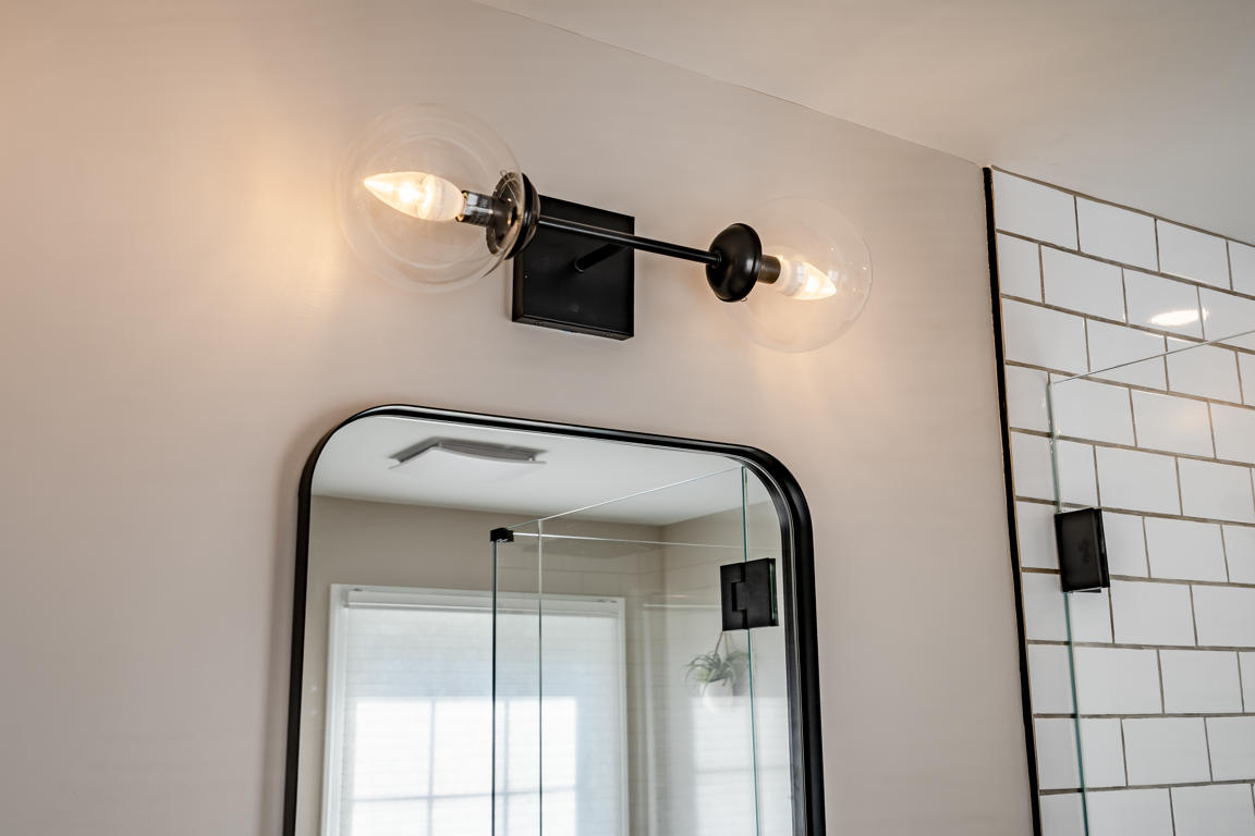 Clear glass globe two-light vanity fixture in matte black finish above rounded-corner mirror with subway tile visible