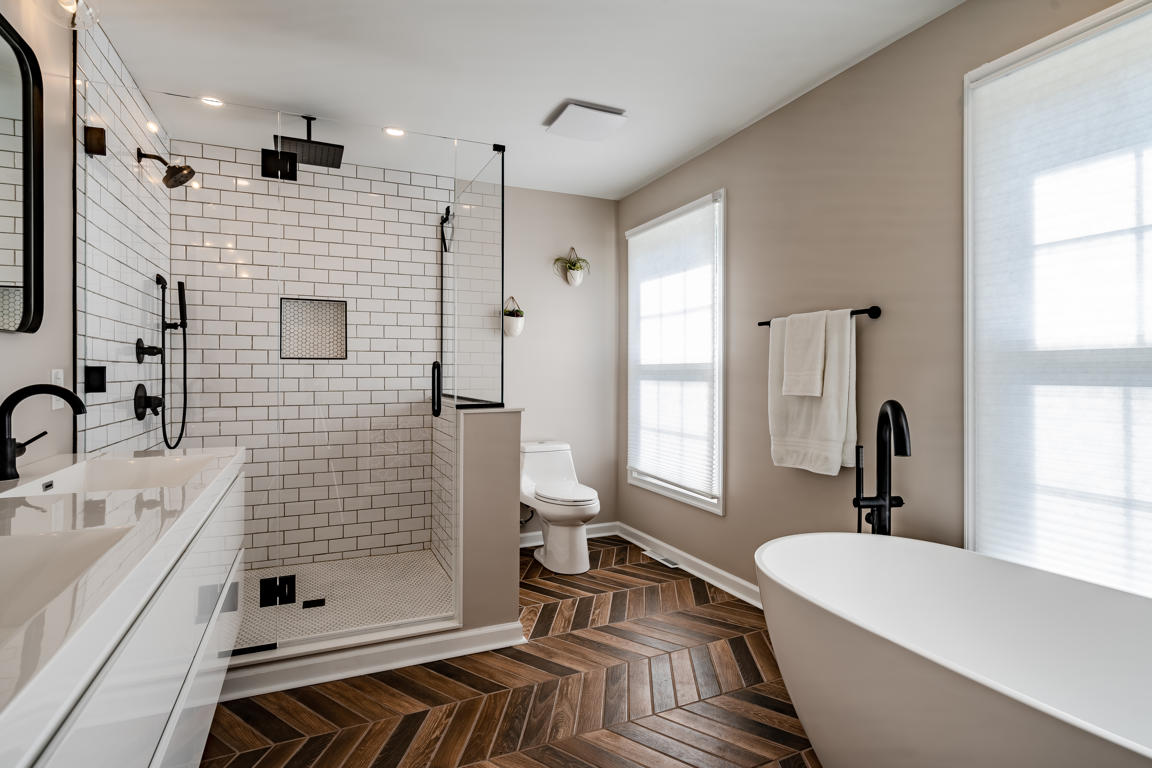 Walk-in shower interior showing white subway tile walls, penny round mosaic niche with black trim, and matte black fixtures
