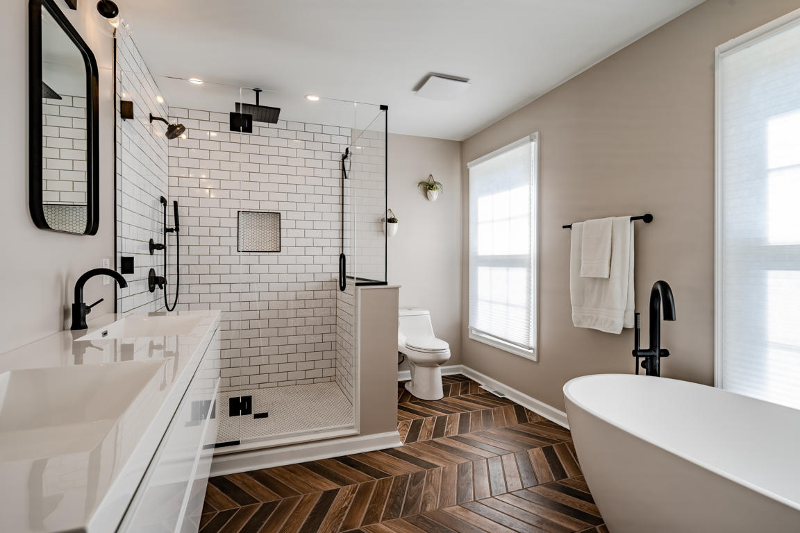 Shower entry detail with frameless glass door, matte black handle hardware, white subway tile, and herringbone floor visible beyond