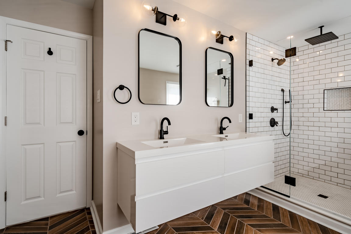 Floating white gloss vanity cabinet with thick white countertop, integrated sink, and matte black faucet on herringbone tile floor