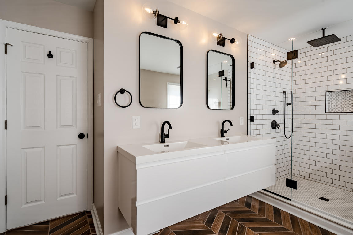 Black-framed rounded-corner mirror above floating vanity reflecting the shower enclosure and tub beyond