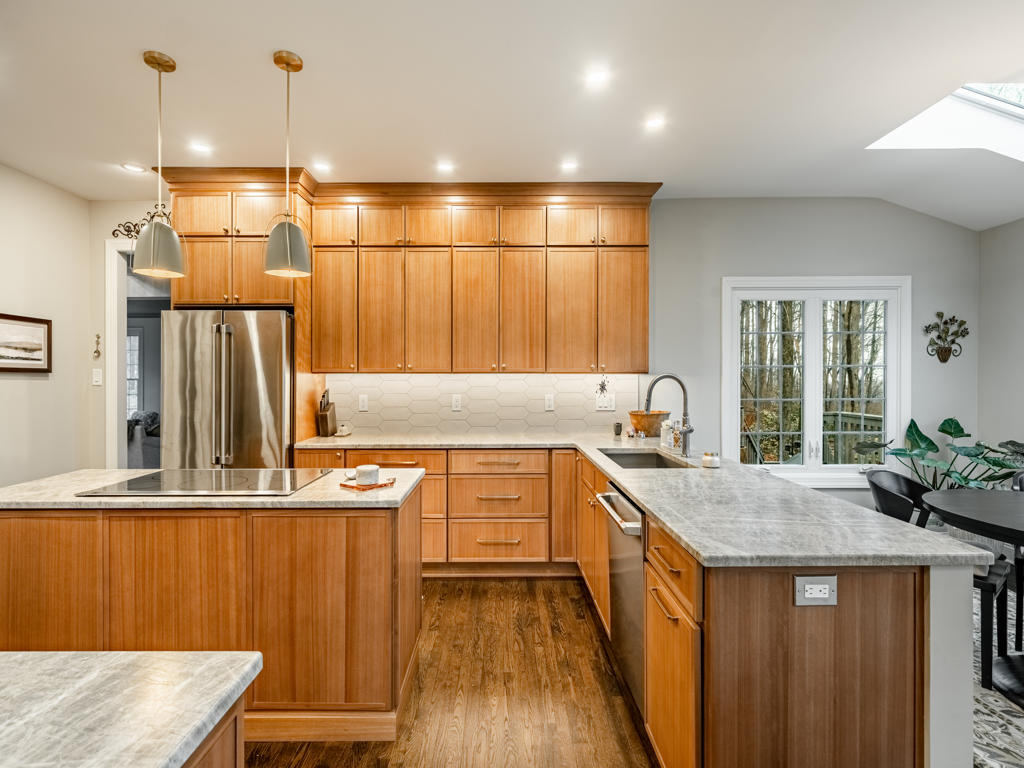 Wide angle overview of West Chester PA kitchen renovation featuring maple shaker cabinets, leathered quartzite countertops, island cooktop, and brushed dome pendants
