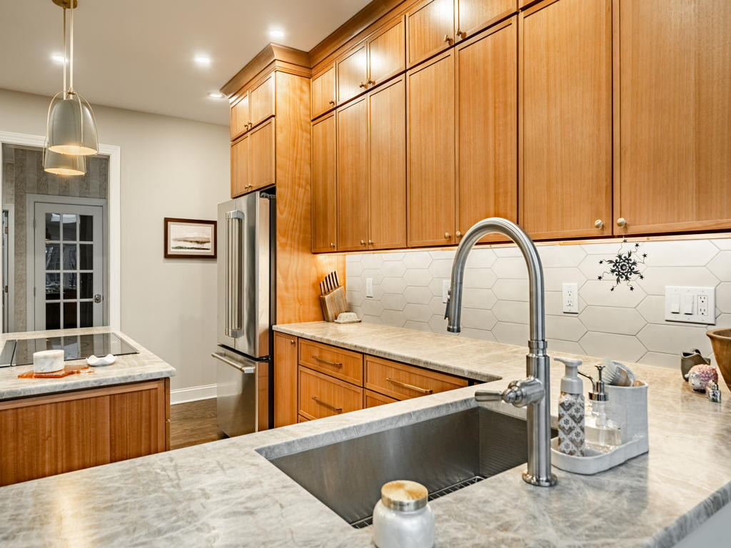 Stainless undermount sink with stainless pull-down faucet set in leathered quartzite countertop with elongated picket tile backsplash and maple shaker cabinetry
