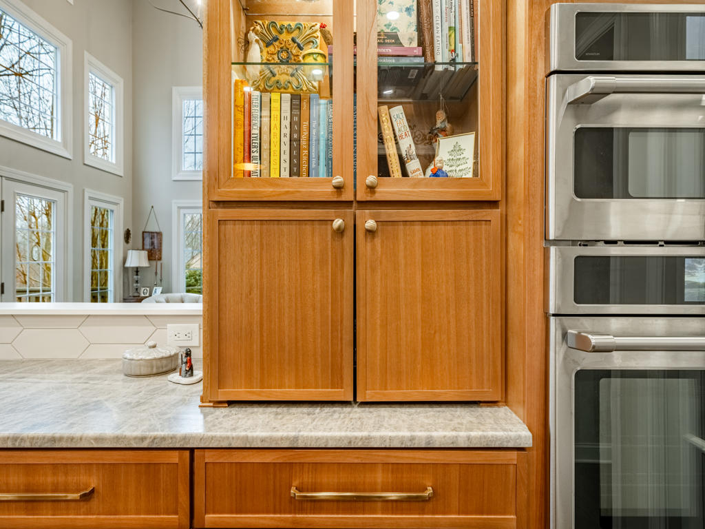 Custom appliance garage doors closed beside glass-front display cabinets and Café double wall oven tower in West Chester PA kitchen