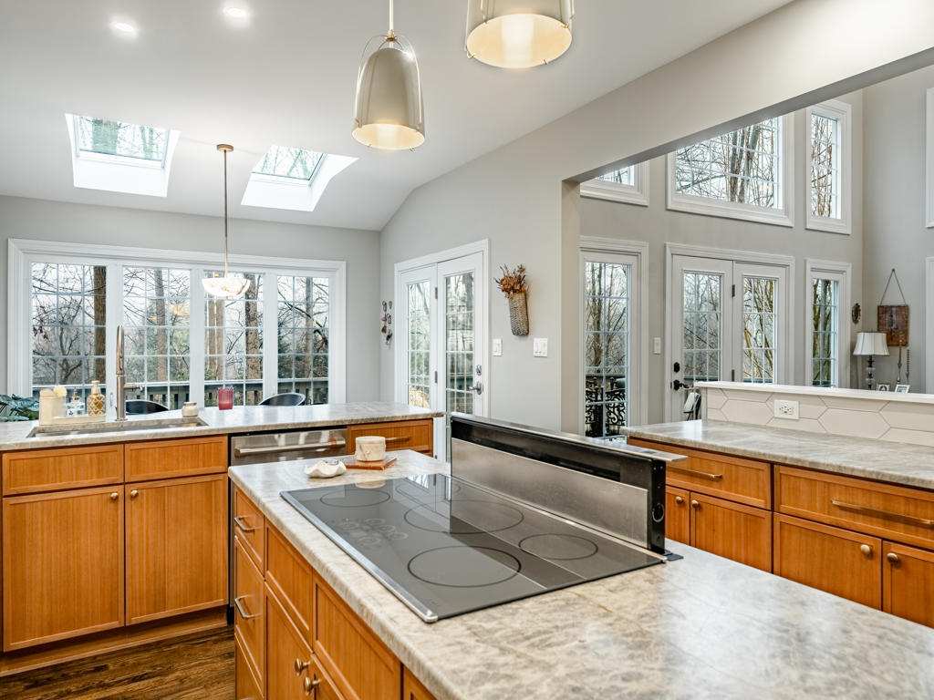 Leathered quartzite island in West Chester kitchen with integrated downdraft cooktop extended, twin skylights overhead, and French doors to dining nook beyond